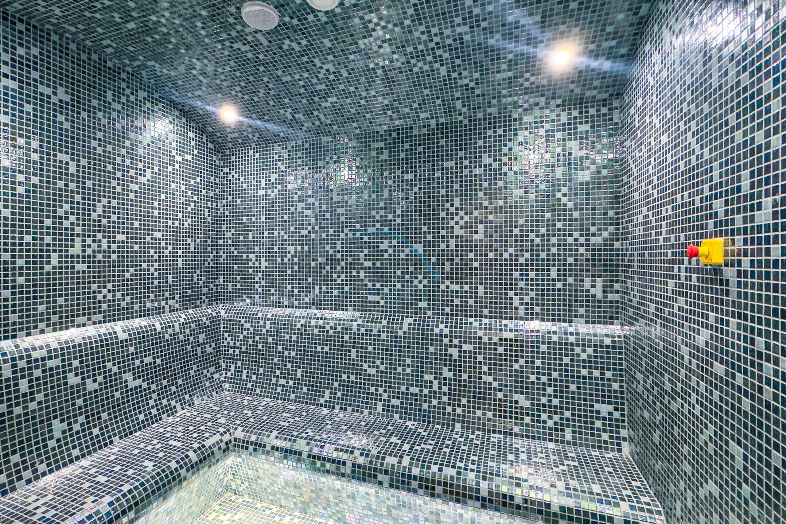 Une pièce carrelée avec une petite piscine dans un coin, un luminaire au plafond et une lumière d’urgence jaune.