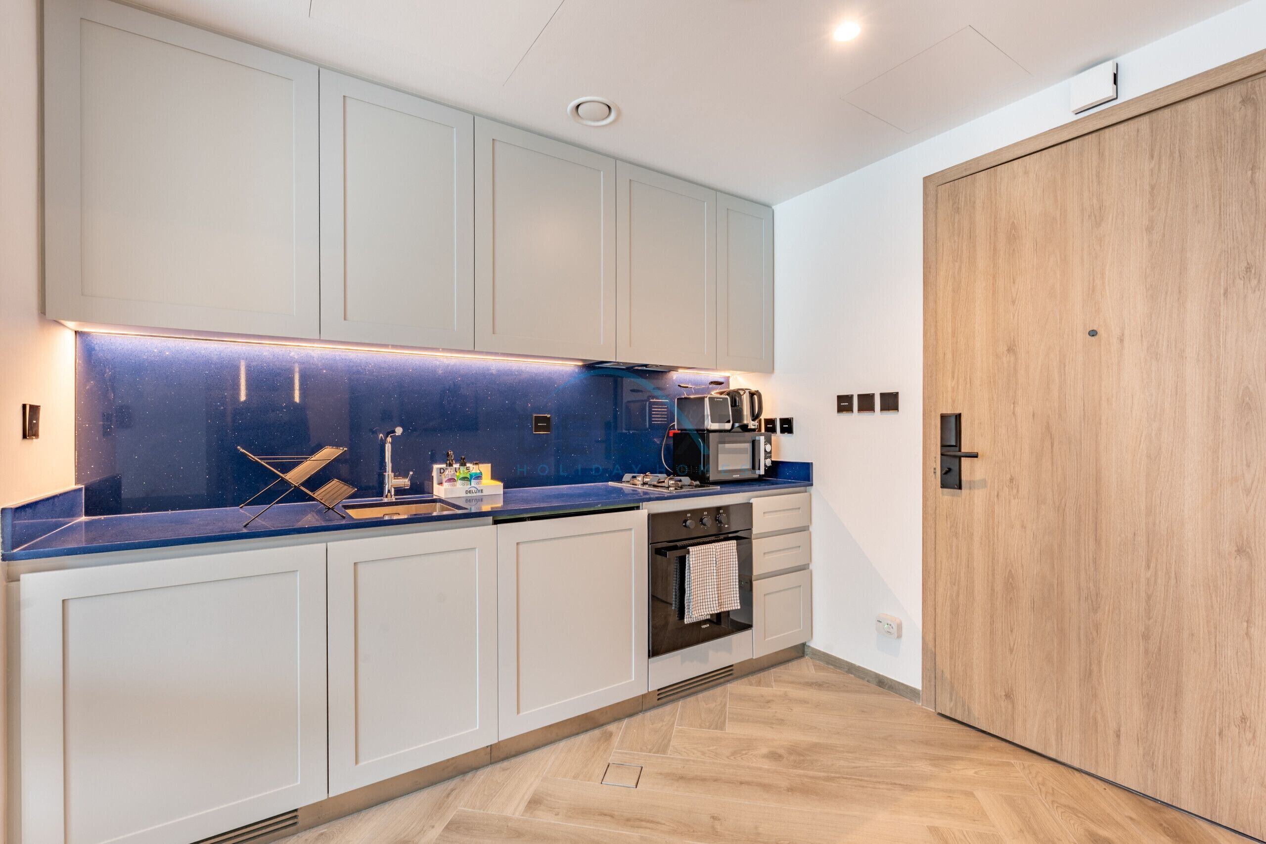 Eine moderne Küche mit weißen Schränken, einer blauen Arbeitsplatte, einer Holztür und einem eingebauten Backofen.