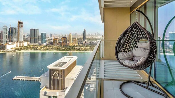 A balcony with a hanging chair, a view of a city skyline, and a body of water. - Luxury 1BR with private Beach Access & Pool, Balcony with Sea View (Dubai)