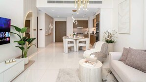A modern living room with a flat-screen TV, a dining area, and a kitchen. - Luxury 1BR with private Beach Access & Pool, Balcony with Sea View (Dubai)