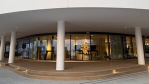 A modern building with a curved facade, large glass windows, and a central open area with seating. - Luxury 1BR with private Beach Access & Pool, Balcony with Sea View (Dubai)