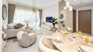 A modern living room with a sofa, dining table, and TV. - Luxury 1BR with private Beach Access & Pool, Balcony with Sea View (Dubai)