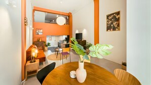 A dining area with a round table, chairs, a vase with a plant, a small table with a lamp, and a kitchen in the background. - Industrial Loft Sukhumvit 3-Bedroom Designer House - 2 Min to BTS Bang Chak (Krung Thep Maha Nakhon)