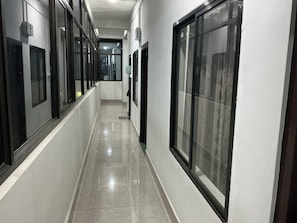 Un pasillo con amplias ventanas, suelo de baldosas y una puerta al final.