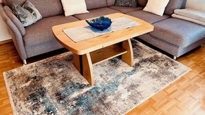 Ett modernt vardagsrum med en grå soffa, ett soffbord i trä och en mönstrad matta.