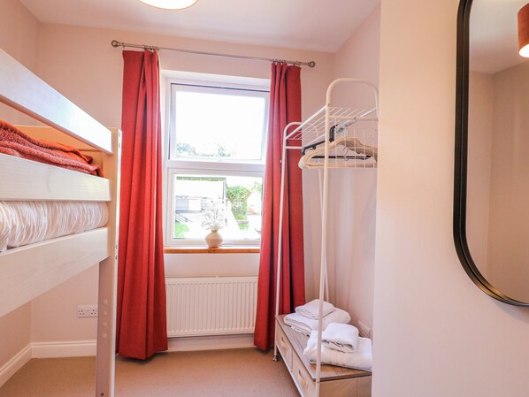A compact hotel room with a bunk bed, a radiator, a window with curtains, a mirror, and a towel rack.