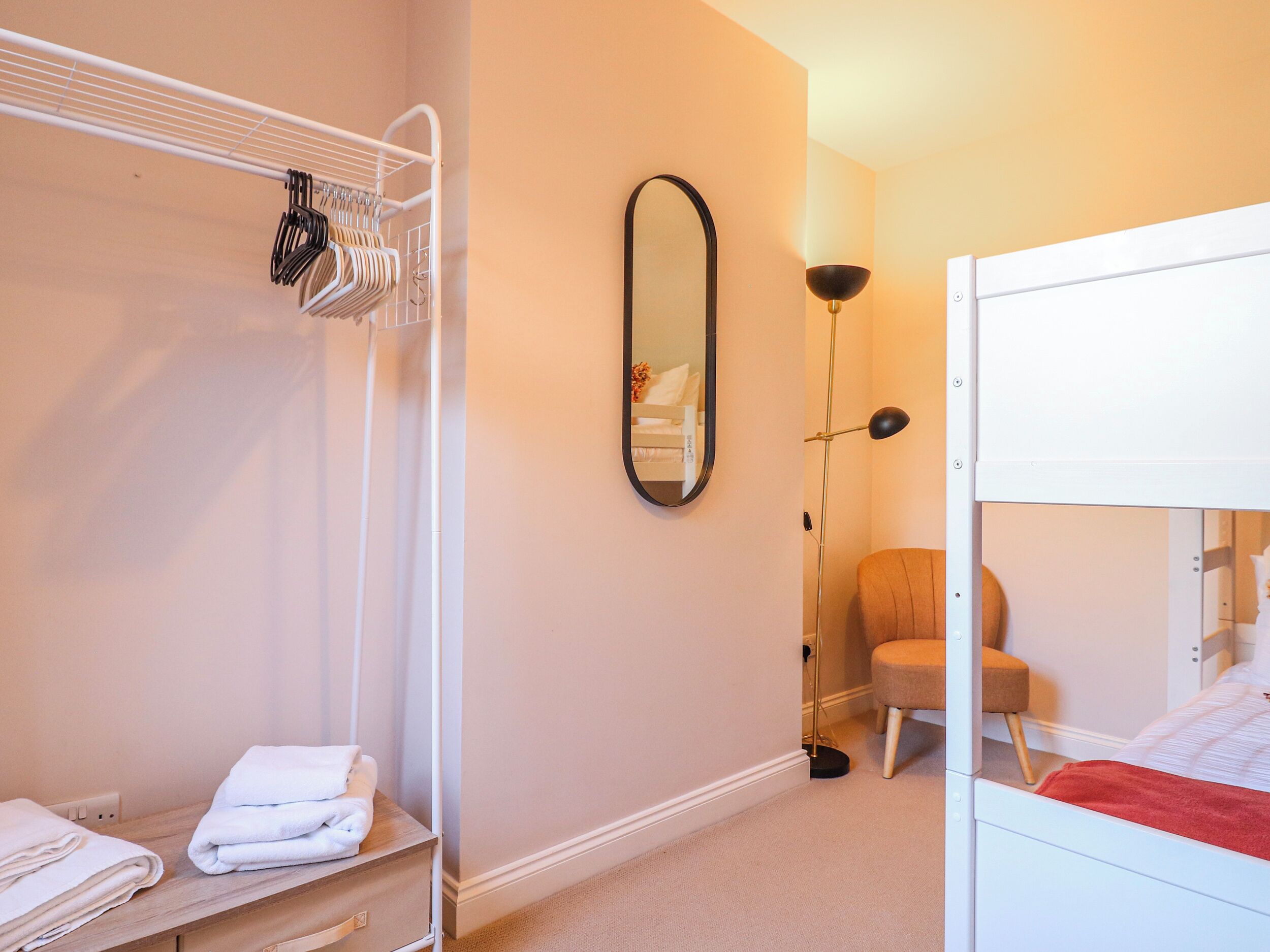 Une chambre avec un lit superposé, une table de chevet avec des serviettes, un miroir, une lampe sur pied et une chaise.