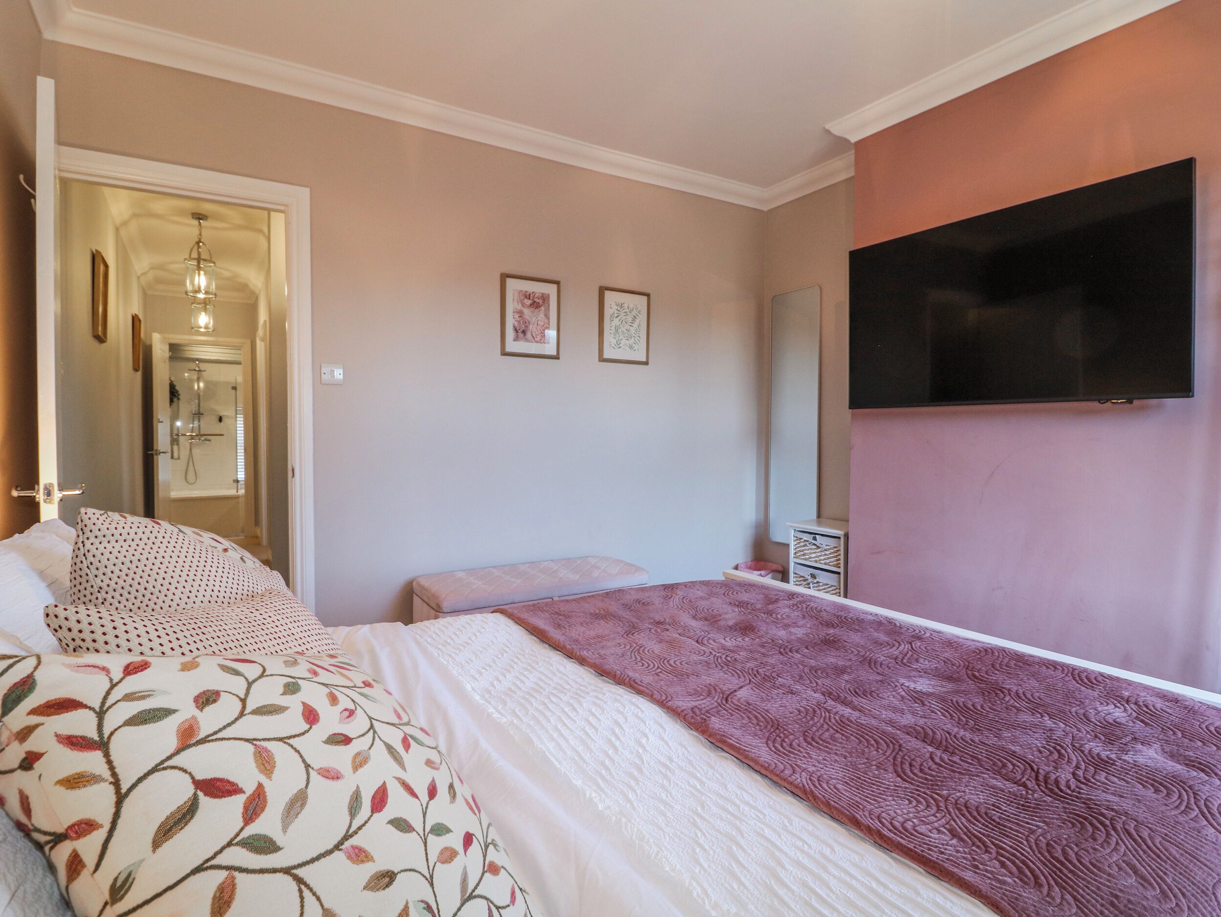Un dormitorio con una cama, una mesita de noche, un espejo y un televisor montado en la pared.