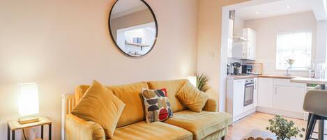 A living room with a sofa, a coffee table, a mirror, and a view into the kitchen.