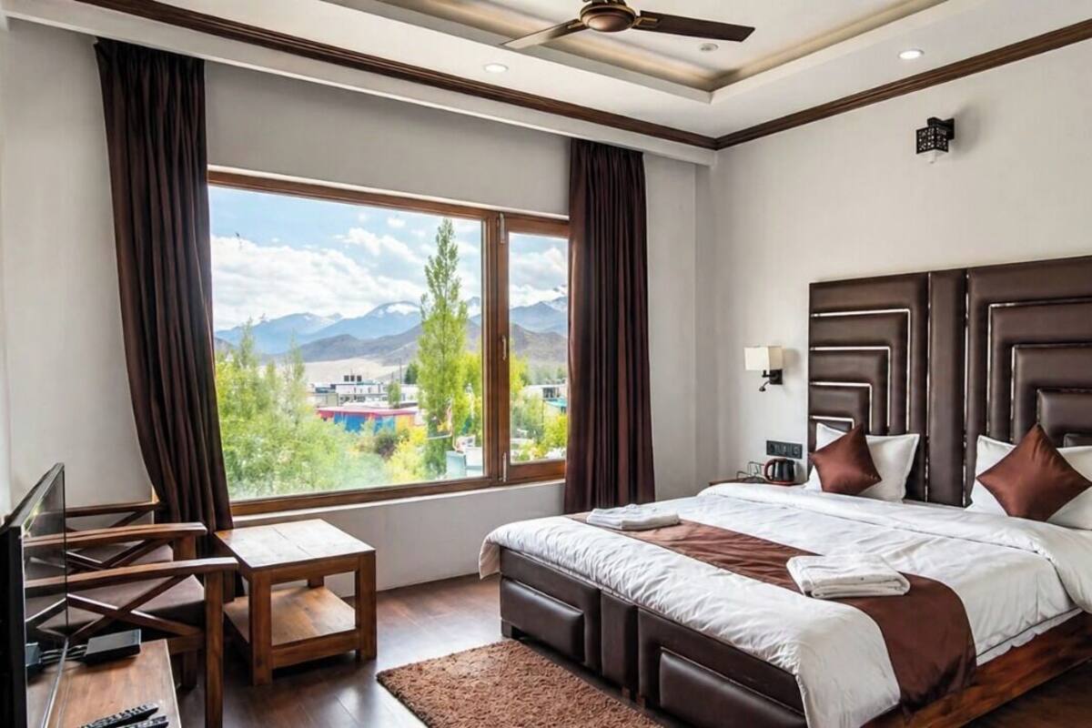 A bedroom with a large window, a bed, a desk, and a ceiling fan.