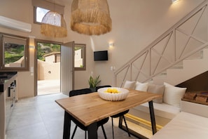 A modern interior with a wooden dining table, black chairs, a white bowl with lemons, a white sofa, and a staircase with geometric design. - Litheos Santorini Luxury Cave Suites (Vourvoulos)