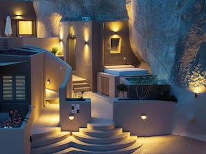 A modern hotel interior with a spiral staircase, multiple light fixtures, and a sign indicating 'The Care Suite.' - Litheos Santorini Luxury Cave Suites (Vourvoulos)