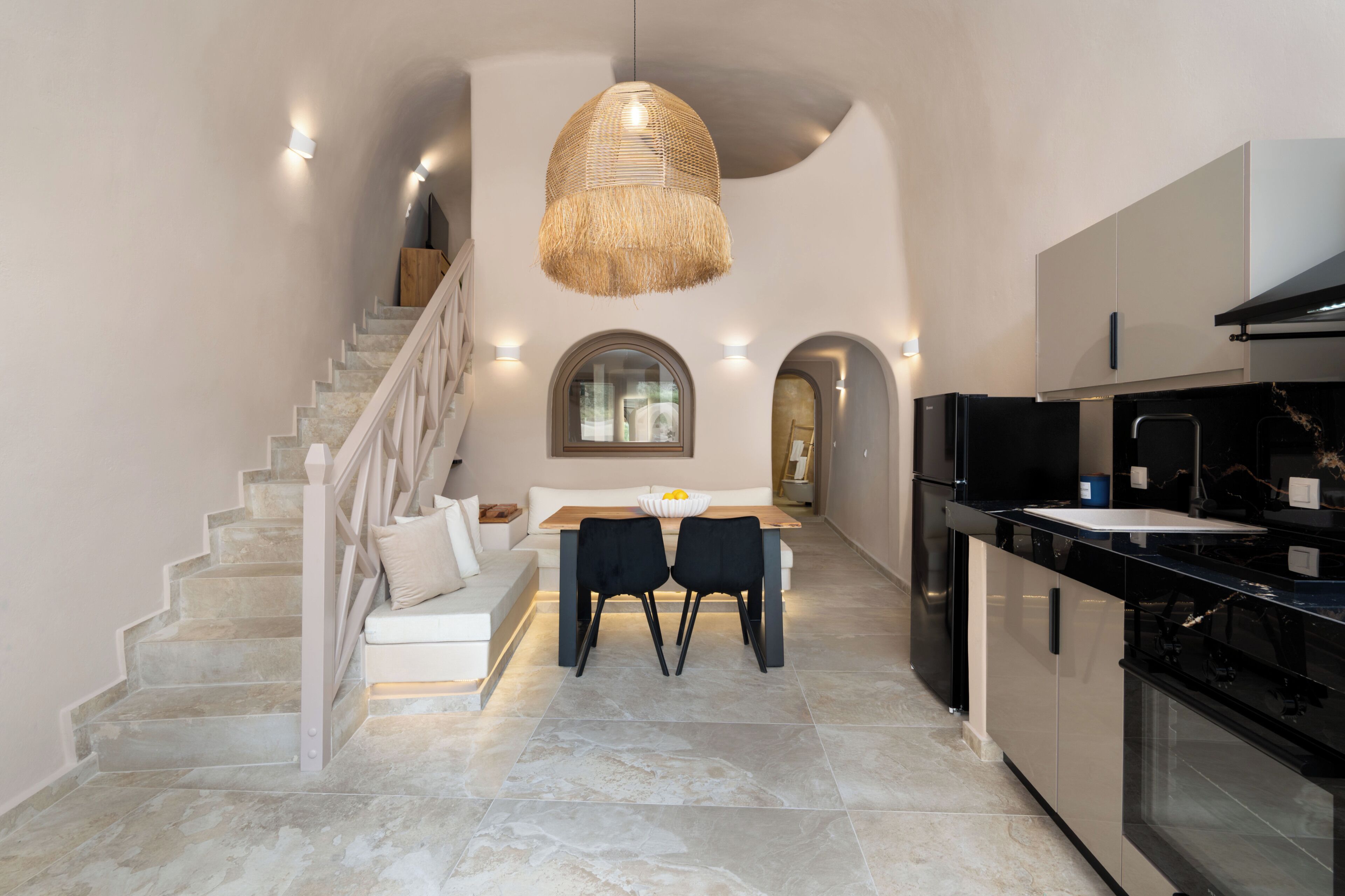 A modern kitchen with a dining area, a staircase, and a large hanging light fixture.