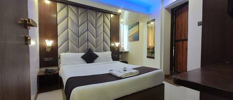 A modern hotel room with a large bed, a nightstand, a wall-mounted lamp, and a ceiling light.