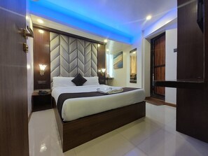 A modern hotel room with a large bed, a built-in headboard, bedside lamps, and a ceiling light. - Hotel Rio (Mumbai)