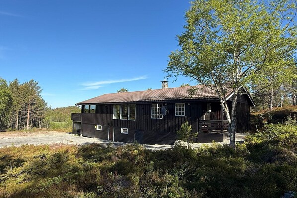 Eine Holzhütte mit Ziegeldach, umgeben von dichtem Wald und blauem Himmel.