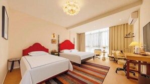 Hotellihuone, jossa on kaksi sänkyä, työpöytä, tuoli, televisio ja ikkuna, jossa on verhot.
