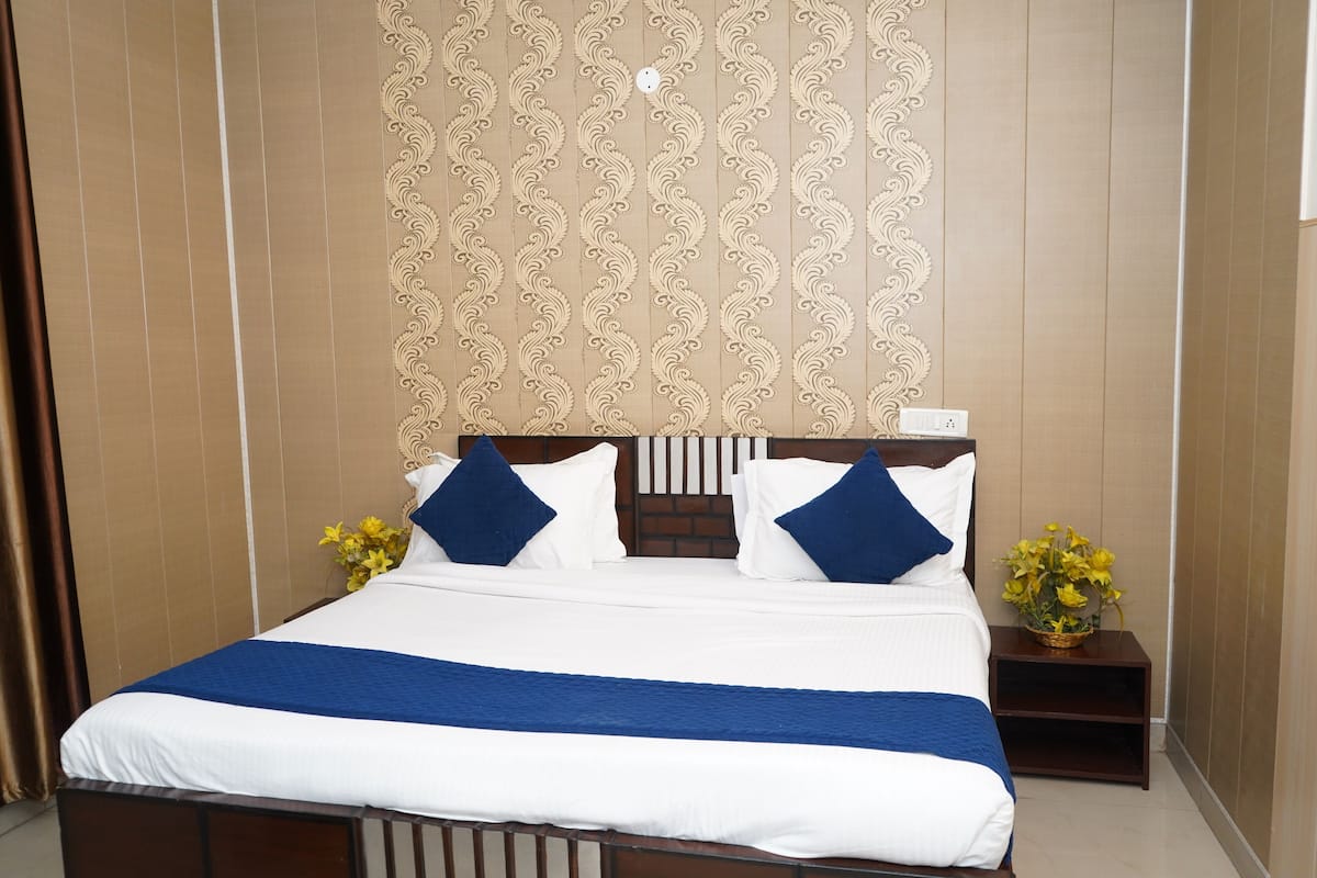 Quarto de hotel com uma cama grande, cabeceira de madeira, parede estampada e mesa de cabeceira com um vaso de flores.
