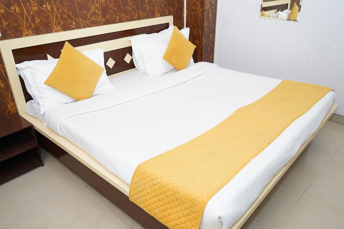 Cama bem arrumada com roupa de cama branca e amarela, cabeceira de madeira e mesa de cabeceira.