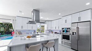 Una cocina moderna con armarios blancos, un refrigerador de acero inoxidable e una isla central con taburetes de bar.