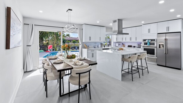 Una cocina moderna con armarios blancos, una isla central y una zona de comedor con sillas.