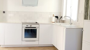 Eine moderne Küche mit weißen Schränken, einem eingebauten Backofen, einem Fenster mit Vorhang und Holzboden.