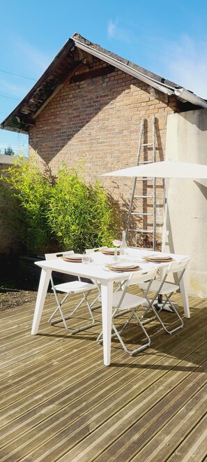 A white table and chairs set on a wooden deck, a brick building in the background, and a ladder leaning against the building. - Detached house - Garden - 1' from the train station - 28' from Paris (Taverny)