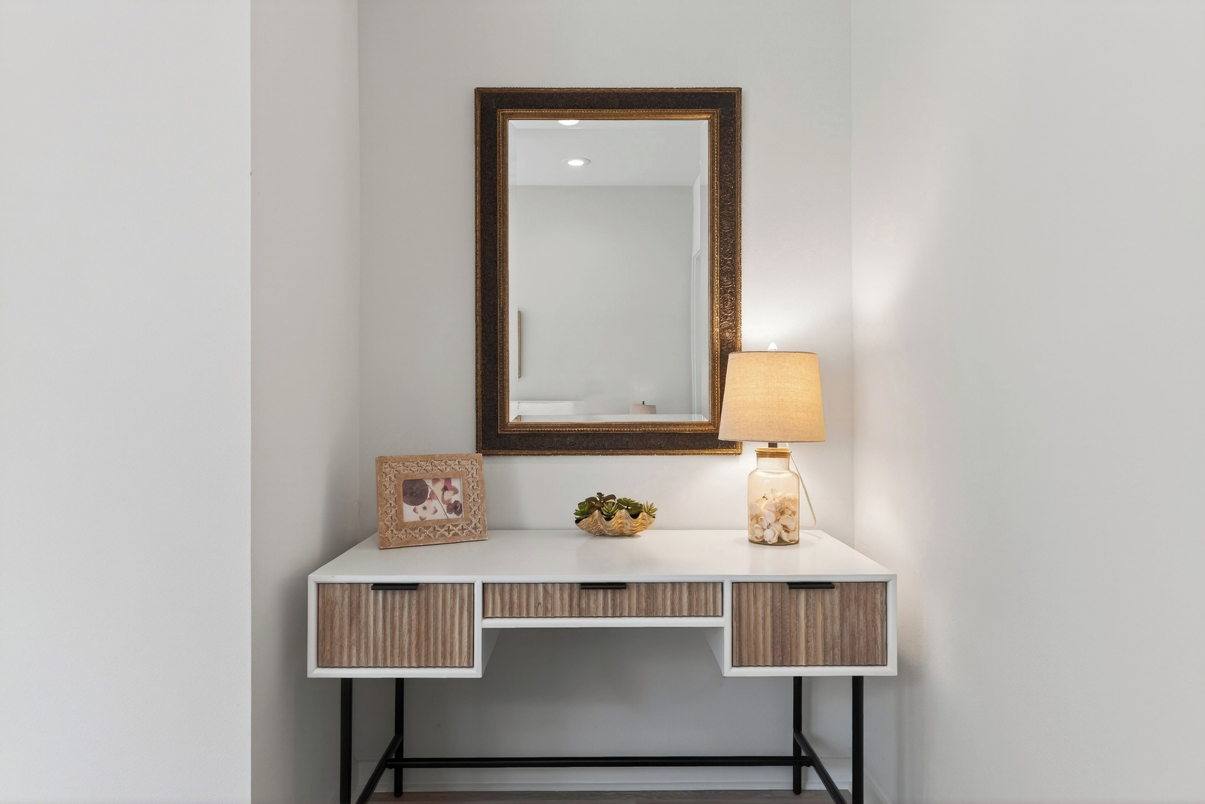 A white desk with a mirror, a lamp, and decorative items.