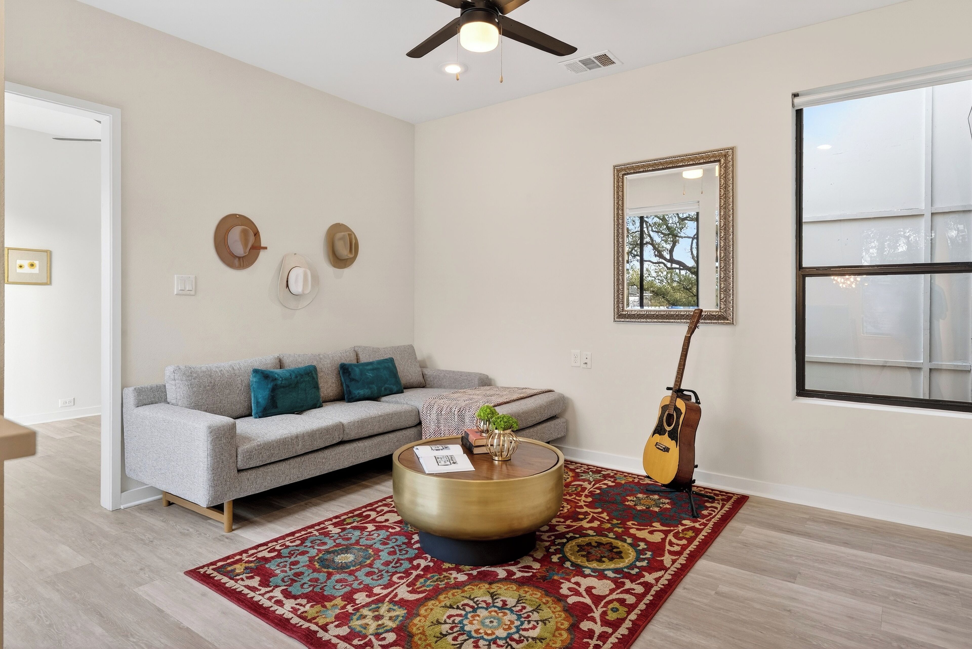 Un salon avec un canapé gris, une table basse ronde, un tapis à motifs, une guitare et un miroir au mur.