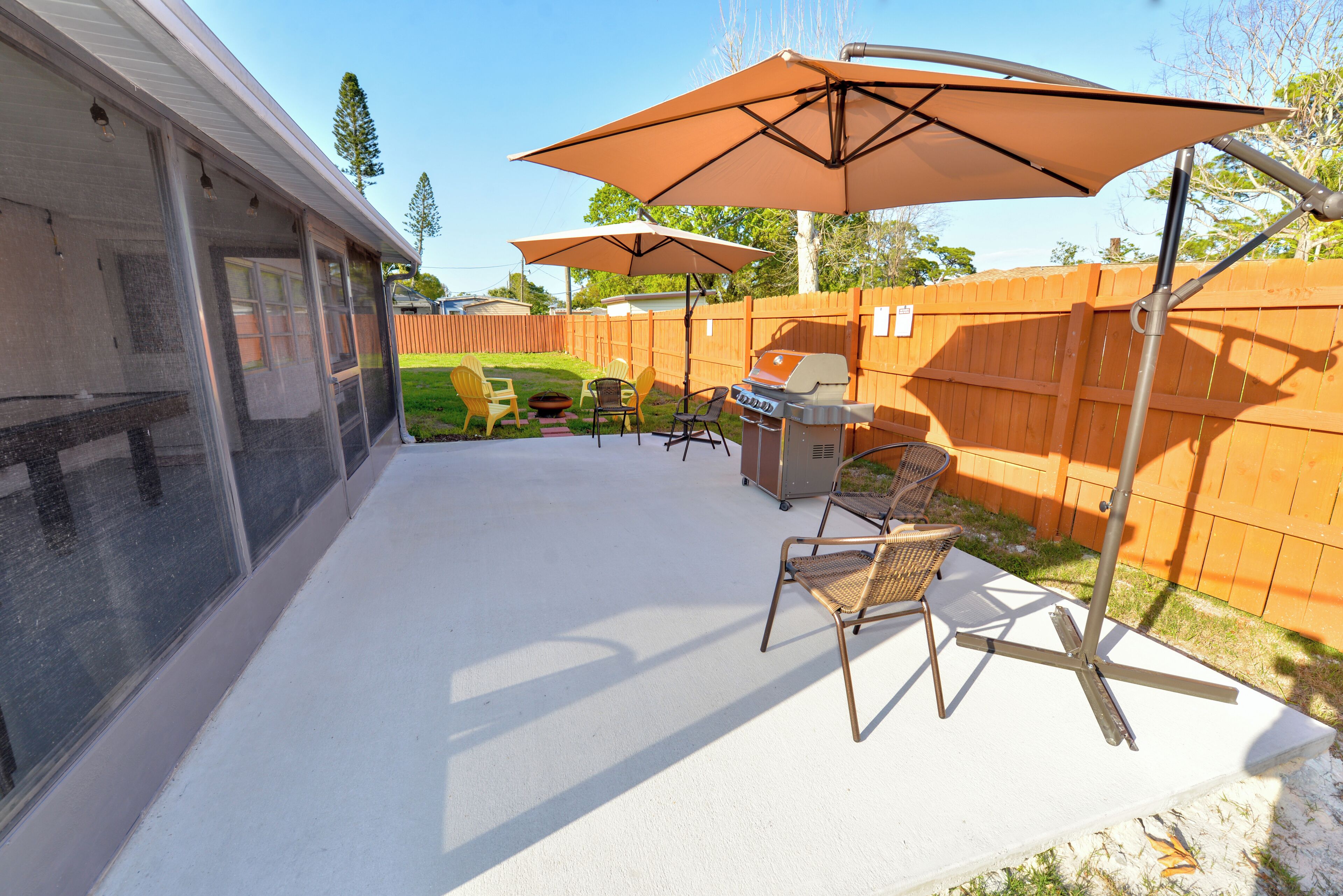 A backyard patio with a grill, chairs, and umbrellas.
