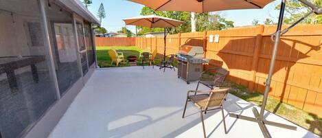 A backyard patio with a grill, chairs, and umbrellas.