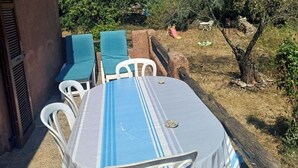 Un área de comedor al aire libre con una mesa y sillas, rodeada de árboles y un muro de piedra.