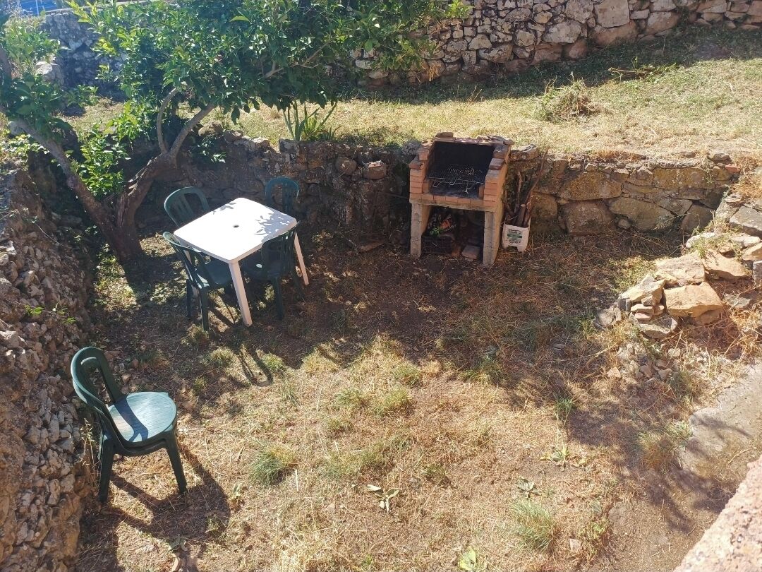 Un espace extérieur aménagé en terrasse, avec un mur en pierre, un barbecue et une table entourée de chaises.