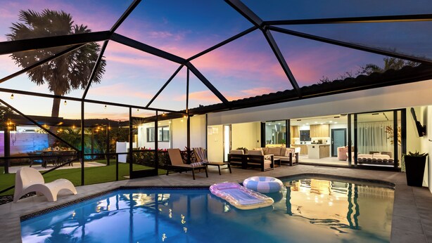 A modern house with a swimming pool, outdoor seating, and a glass-enclosed patio. - Enclosed Pool, Firepit, Outdoor Dining + Bar | 8 Mins to Beach | Soleil Oasis (Fort Lauderdale)