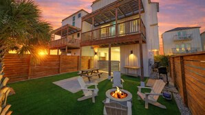 A two-story house with a patio area featuring outdoor furniture and a fire pit. - 4 Coastal Homes • Pools + Golf Cart Boardwalk Access | Dorado Dunes Collective (Port Aransas)