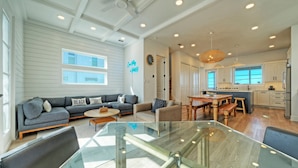 A spacious living area with a glass dining table, a gray sofa, and a wooden dining table with chairs. - 4 Coastal Homes • Pools + Golf Cart Boardwalk Access | Dorado Dunes Collective (Port Aransas)