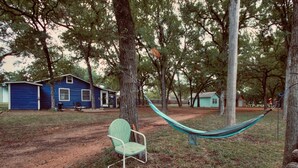 A hammock between trees, a green chair, and a blue house in a wooded area. - Cozy 2-bedroom cabin in peaceful Tow with AC (Tow)
