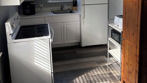 A compact kitchen with white cabinetry, a built-in oven, a microwave, a sink, and a window with blinds. - Cozy 2-bedroom cabin in peaceful Tow with AC (Tow)