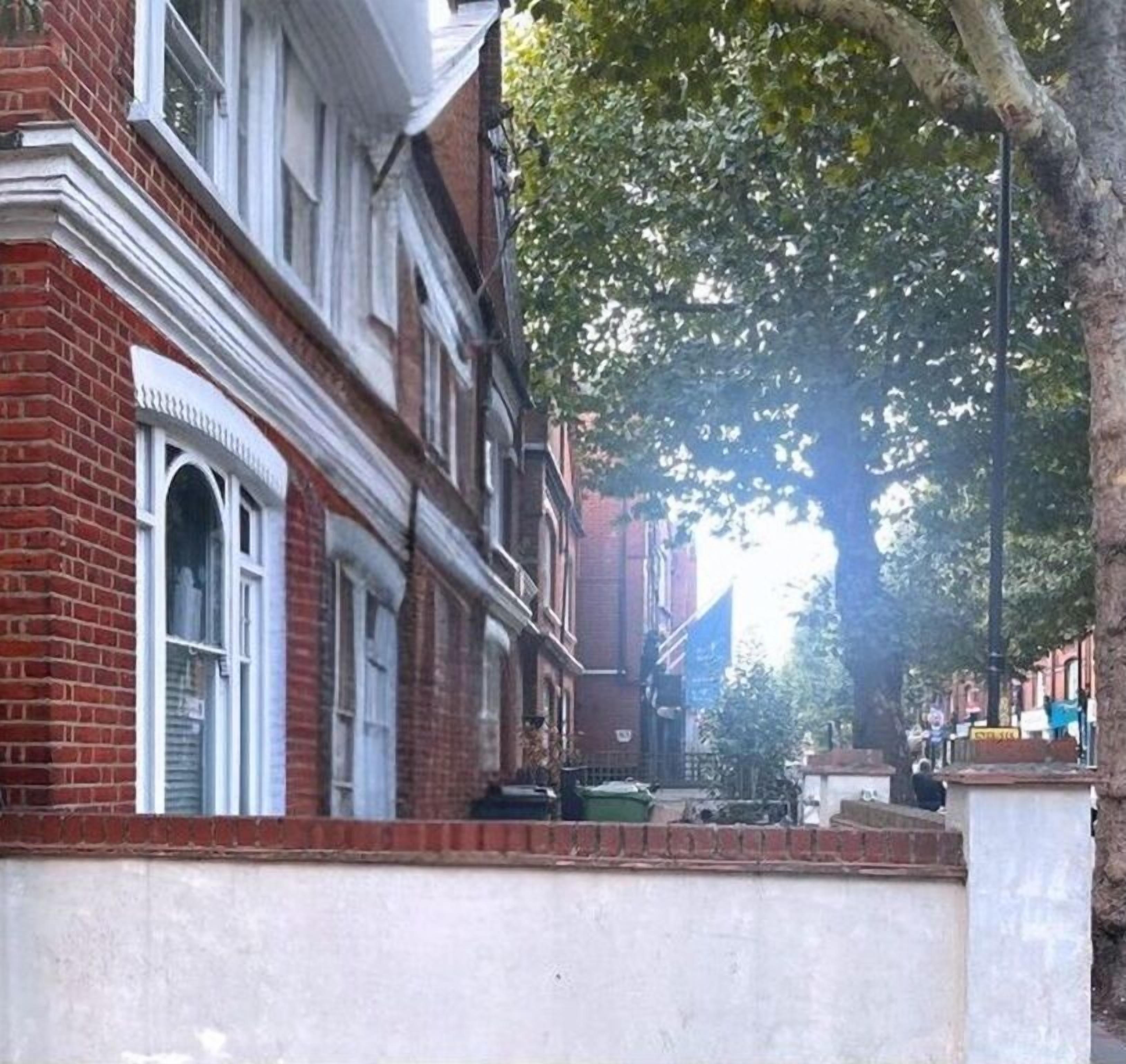 A row of red brick buildings with white window frames and a tree-lined street.