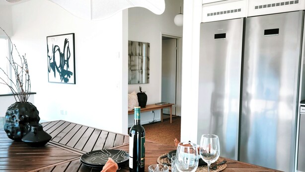 A modern dining area with a wooden table, a wine bottle, and glasses. - Vila Karup Modern Scandinavian Holiday Home (Båstad)