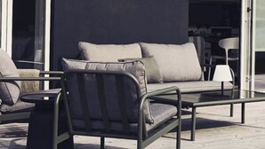 An outdoor seating area with a sofa and chairs, a glass table, and a modern building with a dark facade and large windows. - Vila Karup Modern Scandinavian Holiday Home (Båstad)