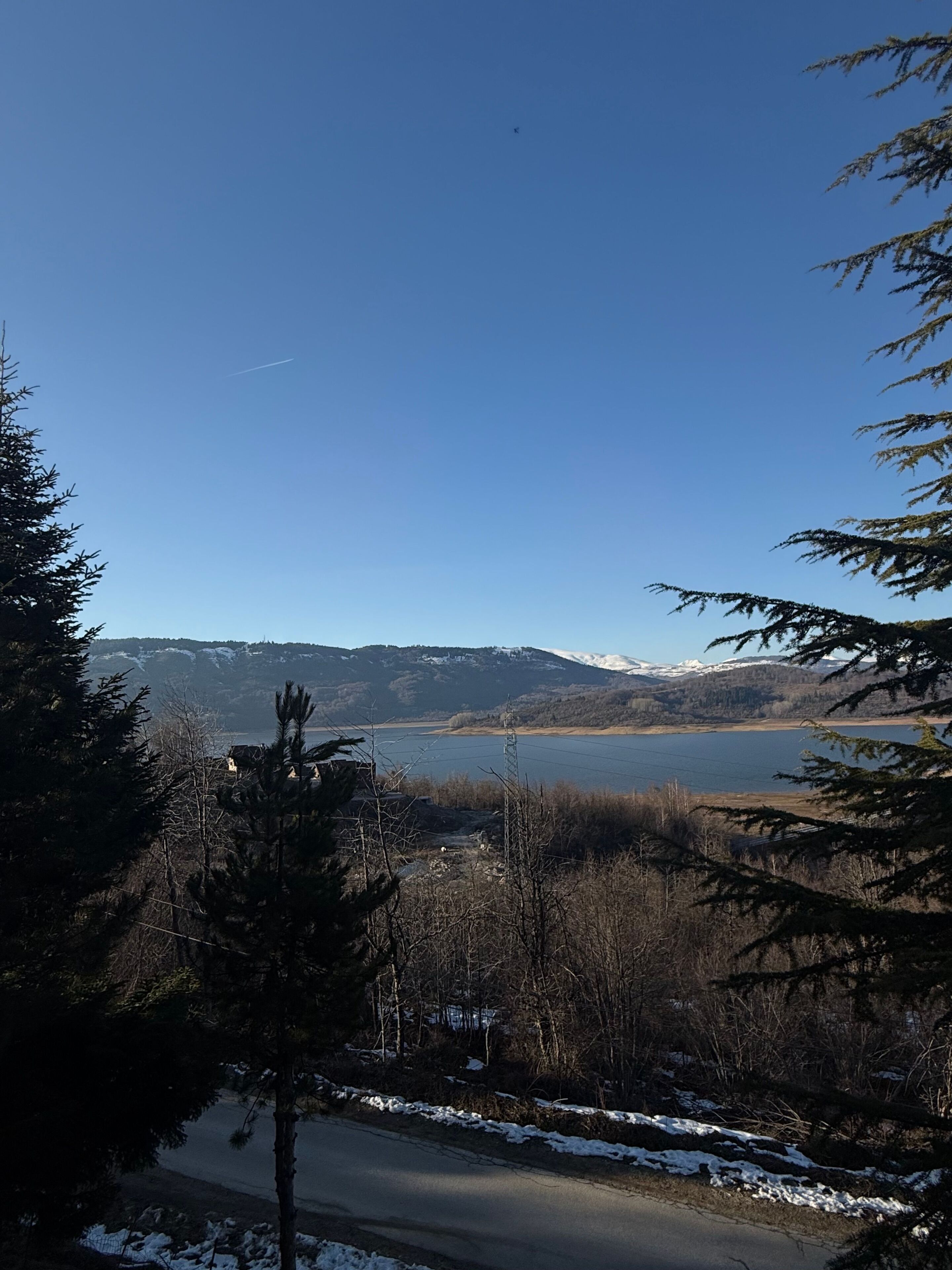 A clear view of a lake, mountains, and a road with snow on the sides.