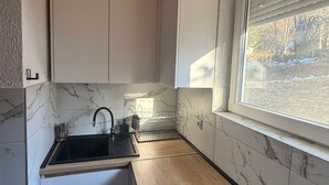 Een kleine keuken met witte kastjes, een houten aanrecht, een spoelbak en een raam met uitzicht op bomen.