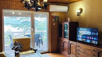 Habitación con paneles de madera, un televisor, un sofá, una mesa de centro y vistas a través de un ventanal.