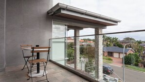 A balcony with a wooden bench, a glass railing, and a view of a residential street.