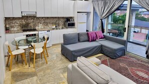 A compact living space with a kitchenette, a dining area with chairs, a sofa with cushions, and a large window with curtains.