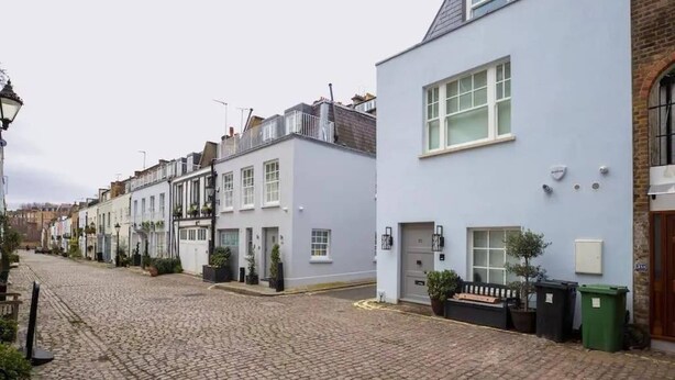 Une rangée de bâtiments blancs, une rue pavée, un lampadaire et un banc.