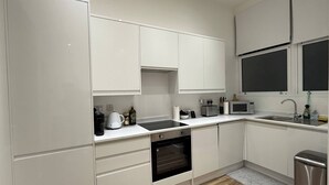 Une cuisine moderne avec des meubles blancs, un four encastré, un four à micro-ondes et un évier.