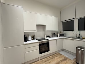 A modern kitchen with white cabinetry, a built-in oven, a microwave, and a sink. - Luxury Apartment in Knightsbridge (Greater London)