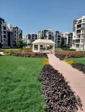 A modern residential complex with a central garden area featuring a gazebo, a paved walkway, and well-maintained greenery. - Elegant Apartment -Sheikh Zayed Compound (Sheikh Zayed)